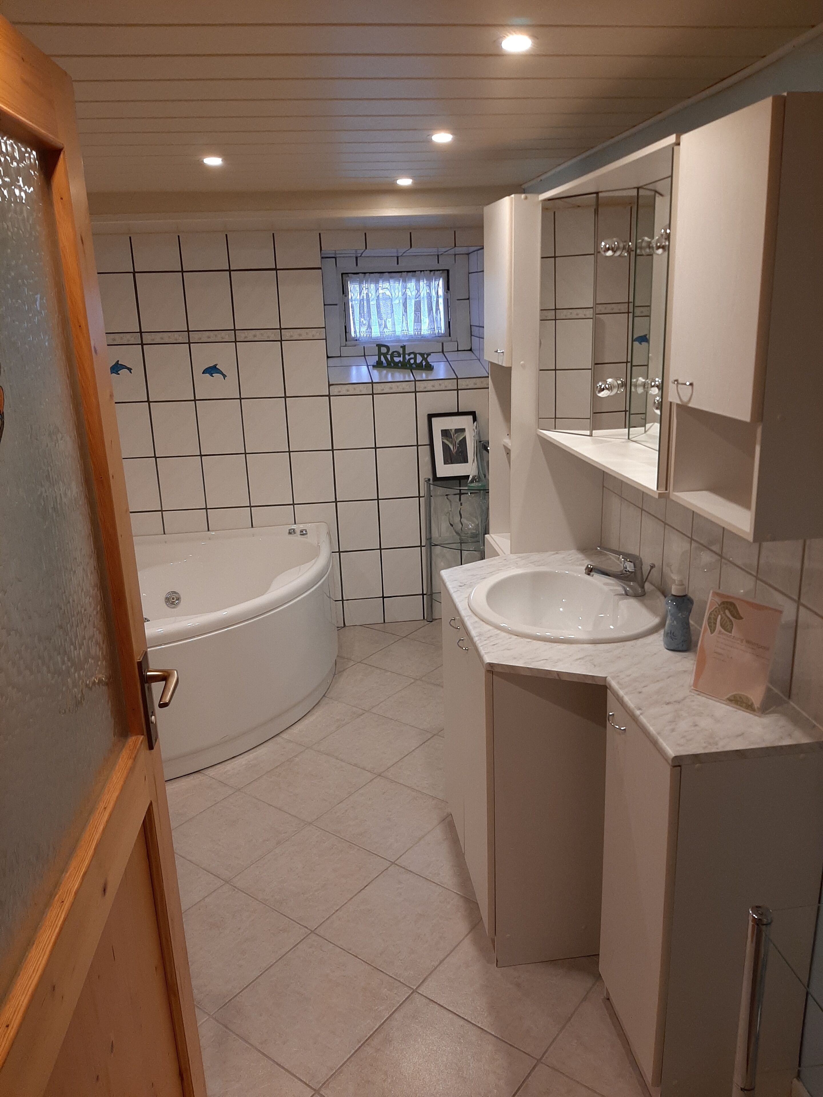 A modern bathroom with a freestanding bathtub, a vanity with a mirror, and a window with a 'Relax' sign.