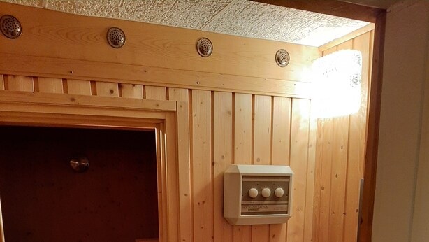 A sauna room with wooden walls, a control panel, and a small table with books and a bottle. - Quietly situated in the Lahn-Dill mountains (Bad Endbach)