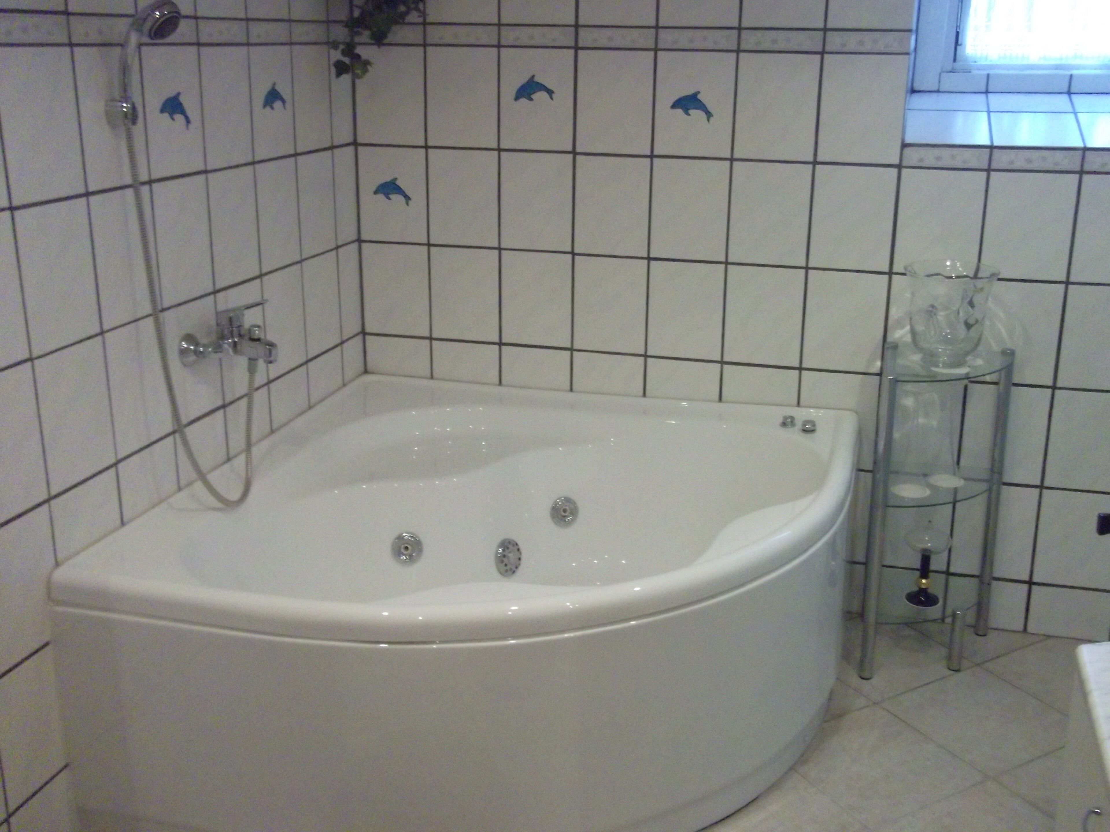 Une salle de bain avec une baignoire blanche, une cabine de douche en verre et des carreaux décorés de motifs de dauphins sur le mur.