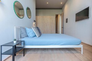 Een moderne slaapkamer met een wit bed, een klein zwart nachtkastje, twee spiegelwanden en een aan de muur bevestigde televisie.