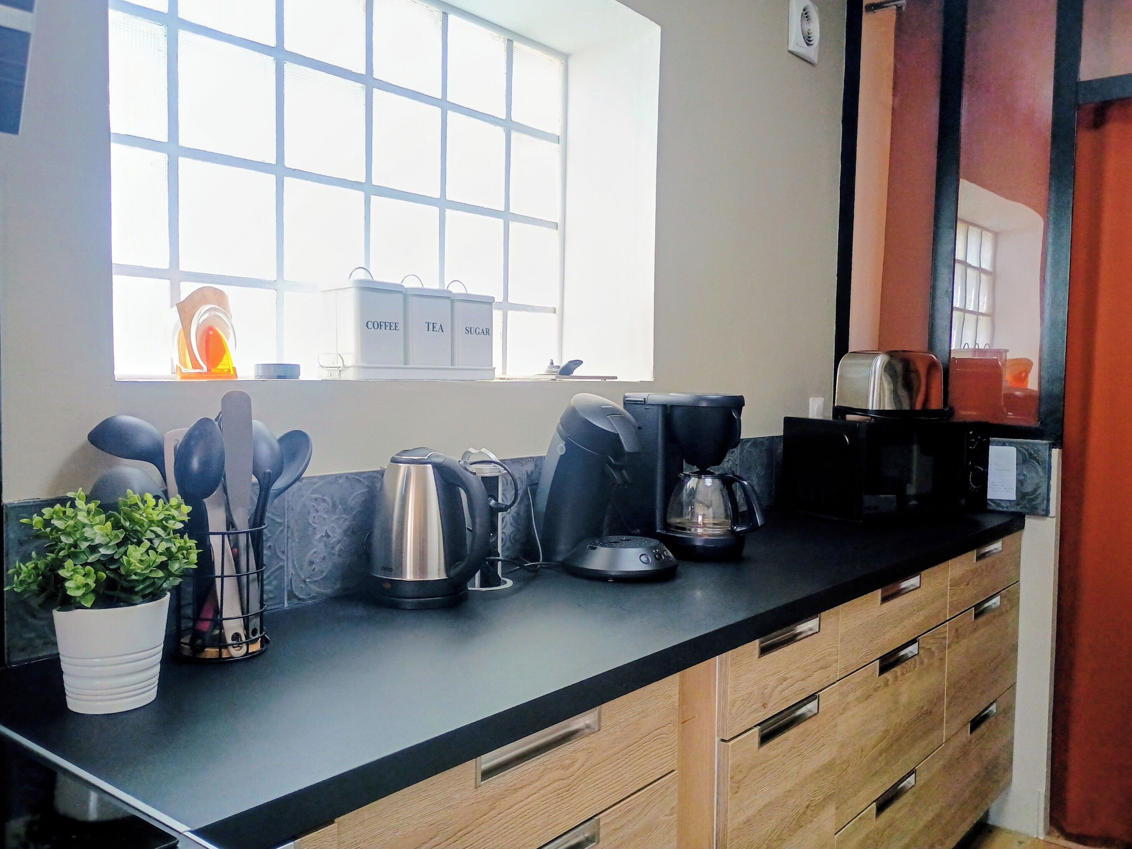 A kitchen with a coffee maker, tea maker, and sugar container on the counter.