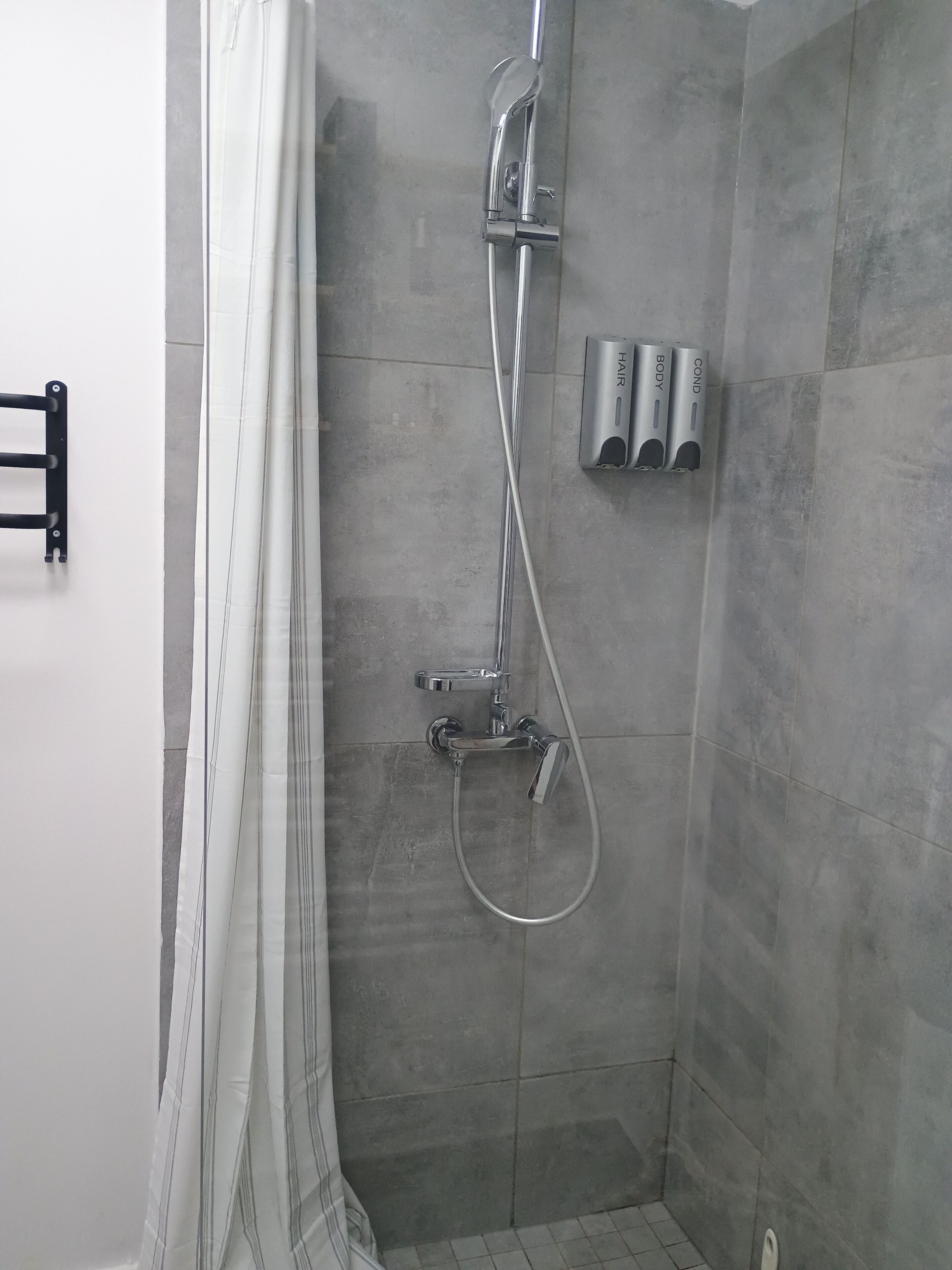 Ducha con cortina, cabezal de ducha de mano y dos dispensadores de jabón en la pared.