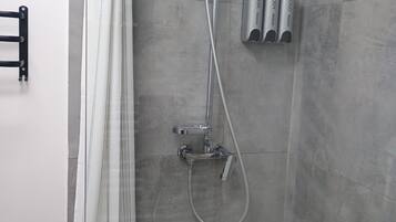 Ducha con cortina, cabezal de ducha de mano y dos dispensadores de jabón en la pared.