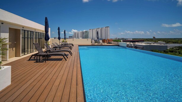 A rooftop pool with lounge chairs and umbrellas, surrounded by modern buildings and a clear sky. - Comfortable with pool and full gym (Cancún)