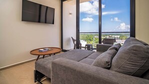 A modern living room with a grey sofa, a small round table, and a TV mounted on the wall. - Comfortable with pool and full gym (Cancún)