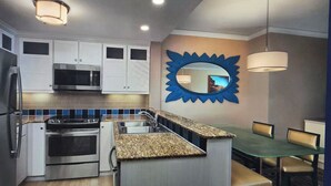 A modern kitchen with white cabinets, a microwave, a stove, and a sink. There is a dining area with a glass table and chairs. - Marriott OceanWatch 2-bedroom villa in Myrtle Beach, SC (Myrtle Beach)