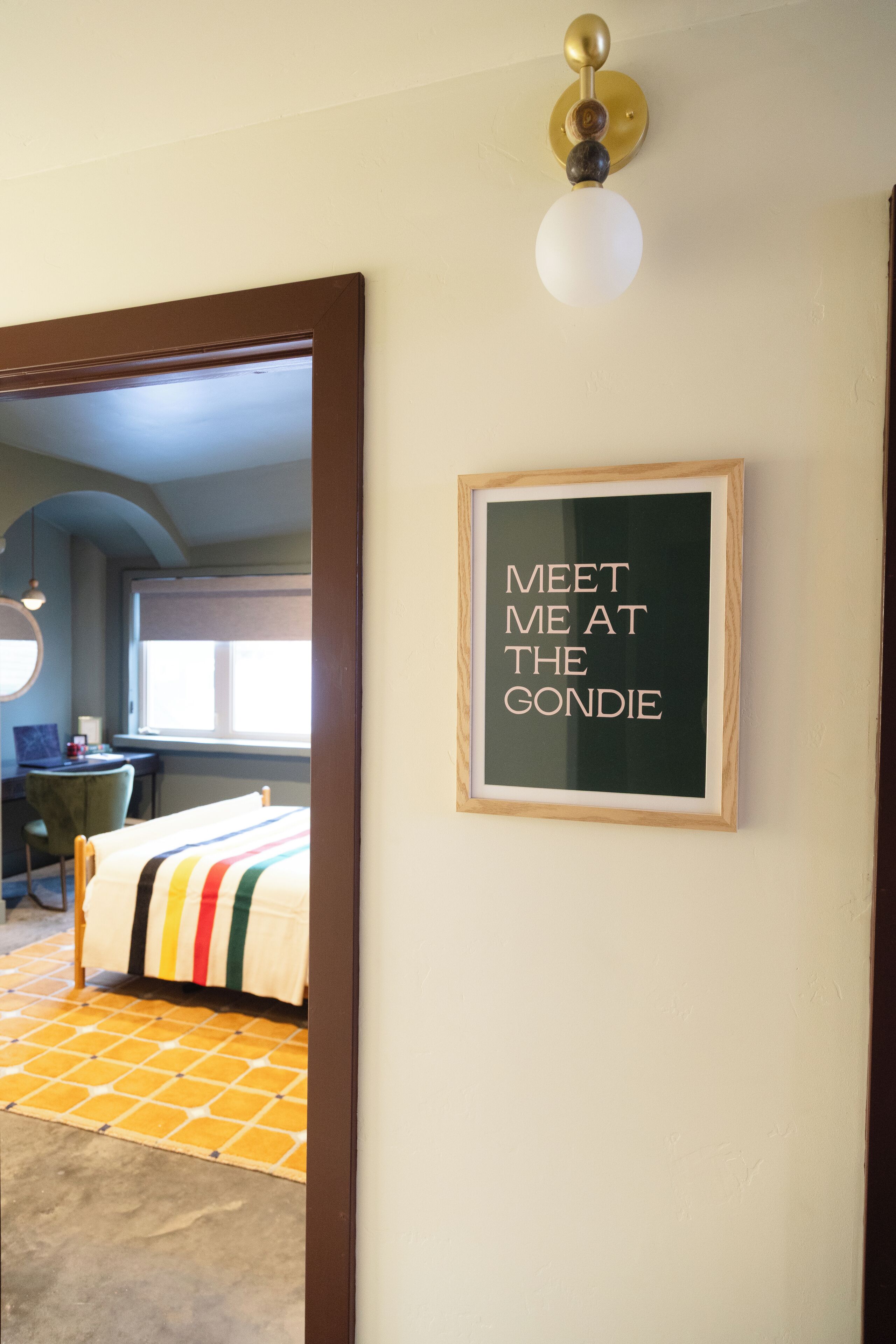 Um quarto com cama, escrivaninha, cadeira e um quadro na parede.