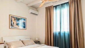 A hotel room with a bed, a painting, an air conditioning unit, a nightstand, and curtains. - An exclusive, quiet home and the terrace of your dreams in the heart of Noto (Noto)