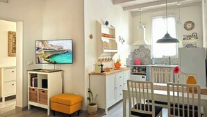 A modern kitchen with a dining area, a television mounted on the wall, and a window providing natural light. - An exclusive, quiet home and the terrace of your dreams in the heart of Noto (Noto)