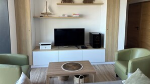 Un soggiorno moderno con una TV a schermo piatto, una console per videogiochi e una libreria. Sono presenti due poltrone verdi e un tavolino in legno.
