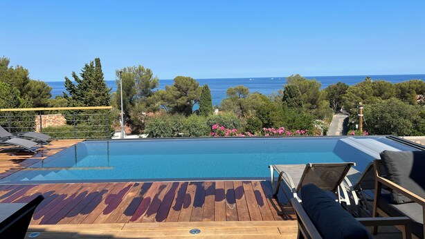 Un terrazzo in legno con piscina, sdraio e vista sul mare.