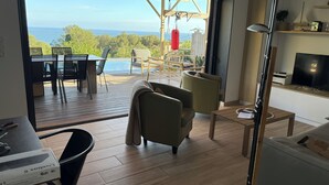 Un soggiorno moderno con un'ampia porta scorrevole in vetro che si apre su una terrazza esterna con piscina e vista sull'oceano.