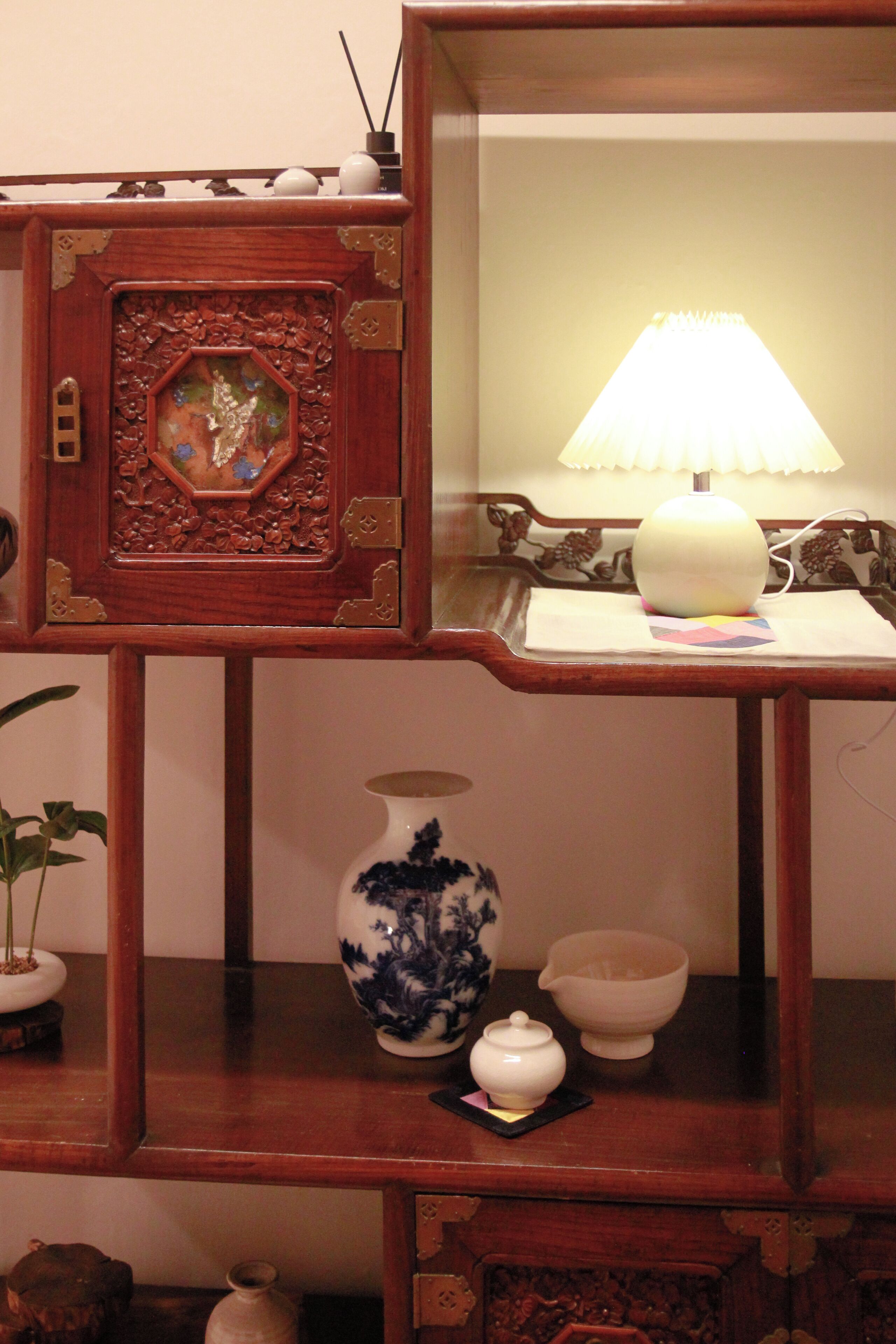 A wooden shelf with a traditional Chinese vase, a small white teapot, and a lamp.