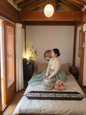 A traditional room with a bed, a wooden ceiling, a bedside table with a lamp, and a mirror on the wall. - moonjarakdalbithanok (Seoul)