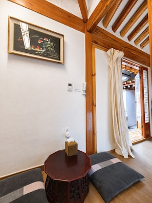 A room with a wooden ceiling, a framed artwork on the wall, a small round table with a box, and a door leading to another room. - moonjarakdalbithanok (Seoul)