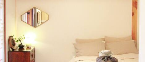 A bedroom with a wooden ceiling, a bed with white bedding, a bedside table with a lamp, and a mirror on the wall.
