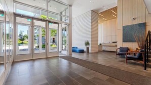 A modern lobby with a reception desk, seating area, and glass doors leading outside.