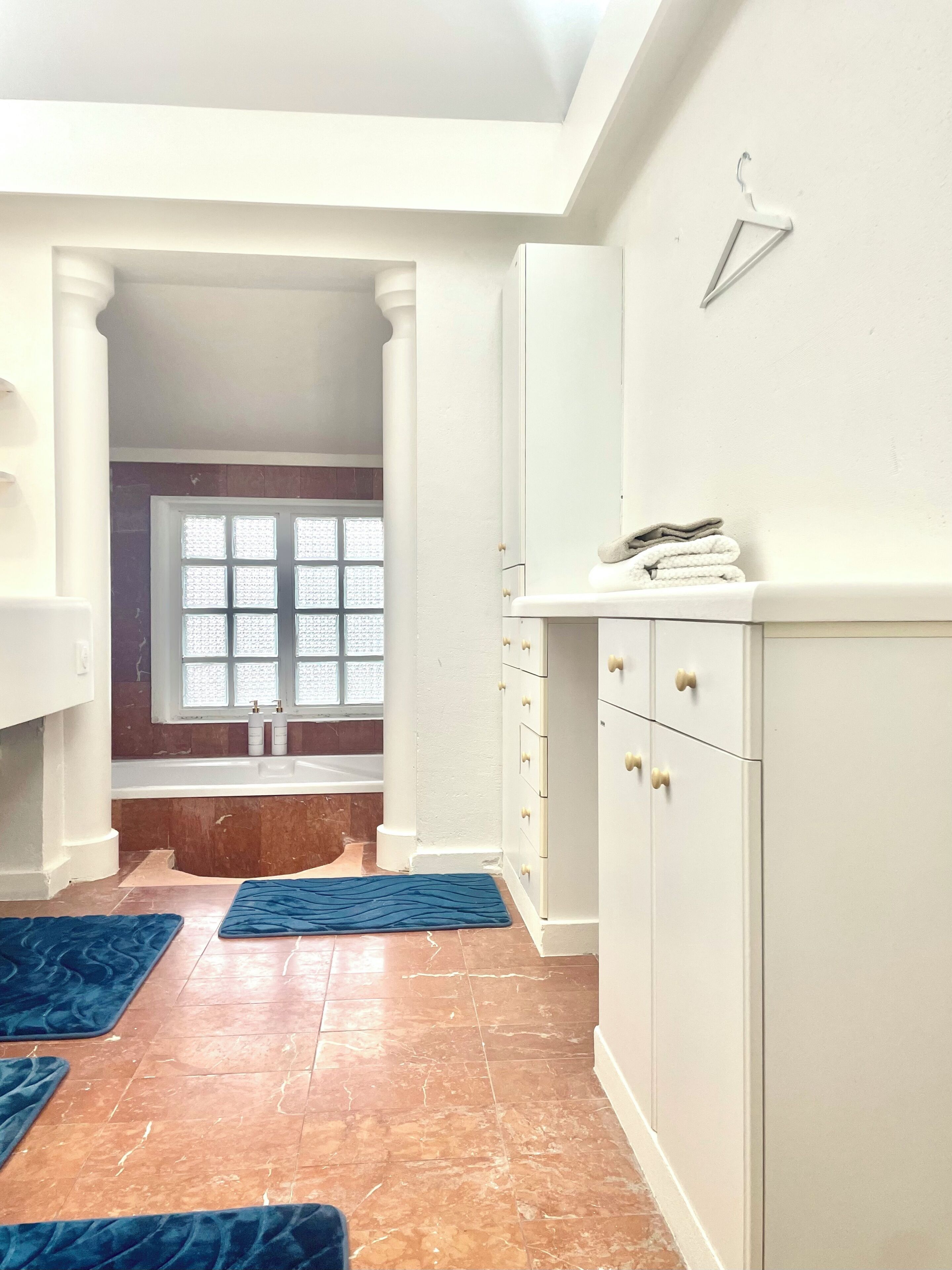 A bathroom with a white vanity, a towel rack, and a window with frosted glass.