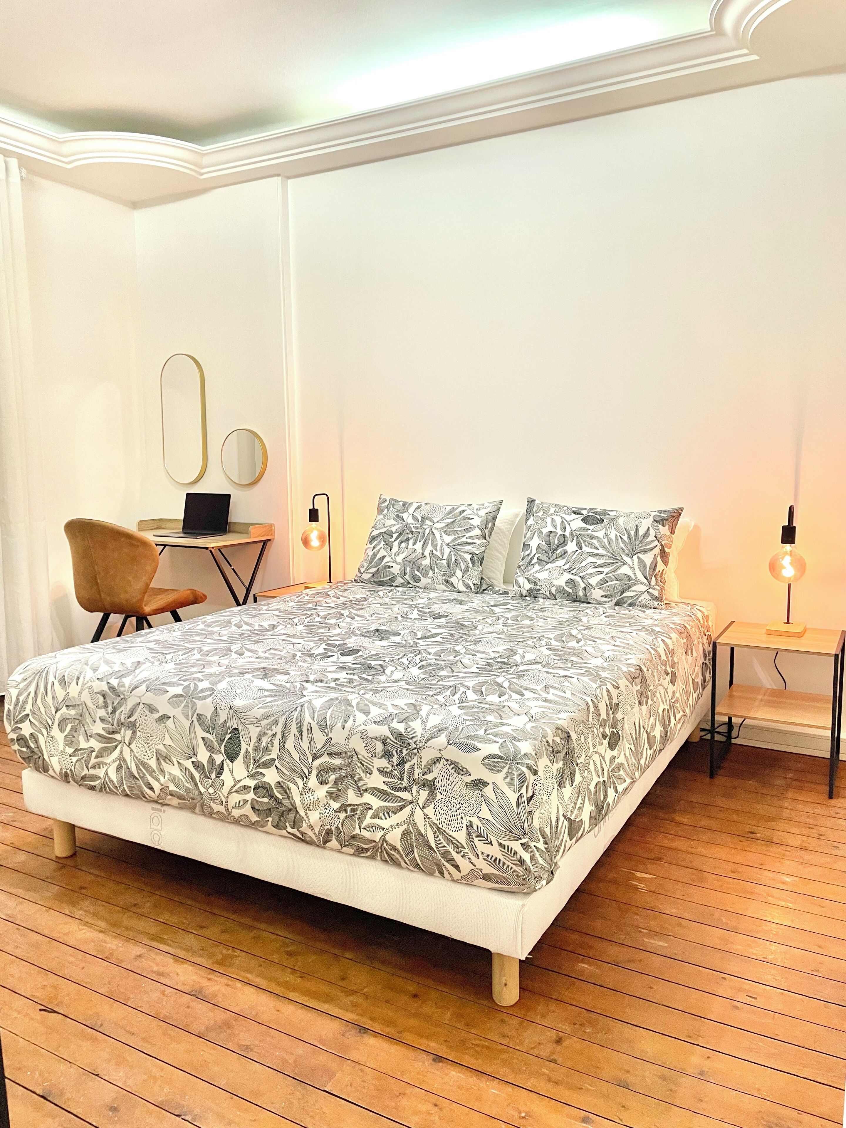 A bedroom with a large bed, a desk with a chair, two wall mirrors, and bedside lamps.