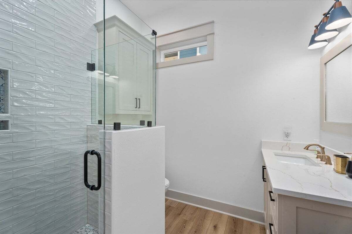 Un bany modern amb una cabina de dutxa de vidre, un moble de tocador blanc amb taulell de marbre i un finestral al sostre sobre el rentapeus.