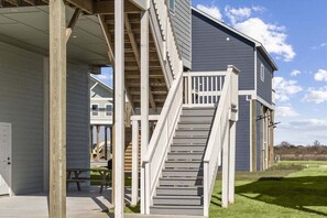 A two-story building with a covered porch and a staircase leading to the upper level. - Beach View | 3BR | Pets | Balcony | Sleeps 7 (Bolivar Peninsula)