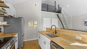 Una cocina moderna con encimera de madera, electrodomésticos de acero inoxidable y una escalera que sube a un nivel superior.