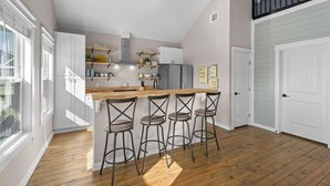 Una cocina moderna con armarios blancos, una barra de madera y taburetes de bar.