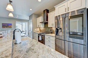A modern kitchen with stainless steel appliances, white cabinetry, and a marble countertop.