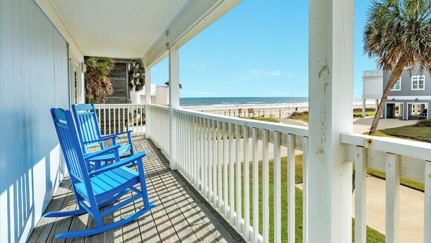 A wooden deck with a rocking chair, a white railing, and a view of the beach. - Great Views from Rooftop Deck, 4th House from Beach, Chill Vibes! (Galveston)
