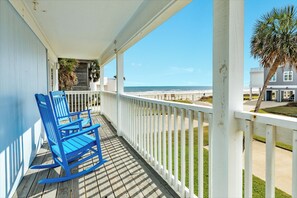 A wooden deck with a rocking chair, a white railing, and a view of the beach. - Great Views from Rooftop Deck, 4th House from Beach, Chill Vibes! (Galveston)