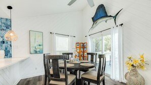 A dining area with a round table, dark wooden chairs, a decorative fish on the ceiling, and a bookshelf with colorful books. - Great Views from Rooftop Deck, 4th House from Beach, Chill Vibes! (Galveston)