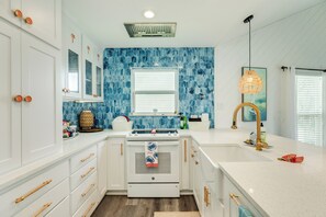 A kitchen with white cabinets, a stove, a sink, and a window with blinds. - Great Views from Rooftop Deck, 4th House from Beach, Chill Vibes! (Galveston)