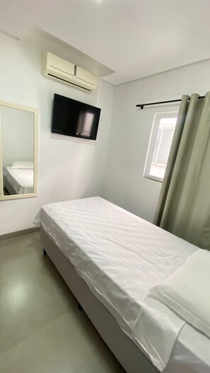 A bedroom with a single bed, a mounted television, an air conditioning unit, and a window with curtains. - HOTEL ZAGONEL  (Chapecó)