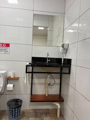 A bathroom with a sink, mirror, towel rack, toilet paper, and a trash bin. - HOTEL ZAGONEL  (Chapecó)