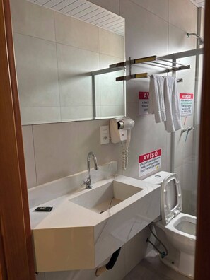 A modern bathroom with a sink, toilet, and a hand dryer. There are towels hanging on a rack and a sign indicating water conservation. - HOTEL ZAGONEL  (Chapecó)