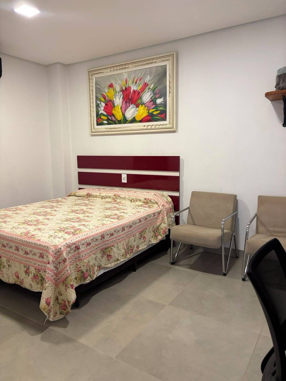 A room with a bed, a chair, a painting on the wall, and a shelf.