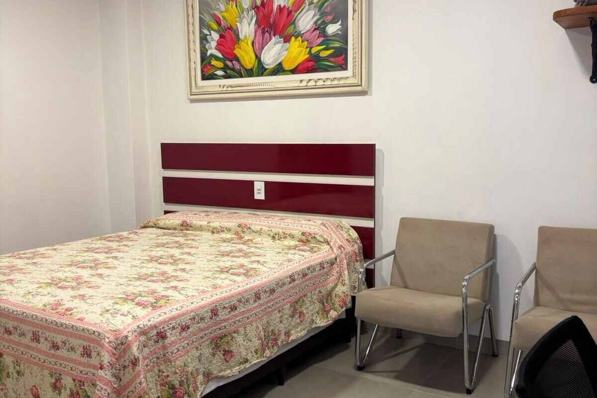 A room with a bed, a chair, a painting on the wall, and a shelf.
