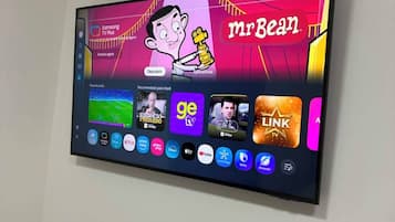 A flat-screen TV mounted on a wall with a selection of streaming apps and a cartoon character.