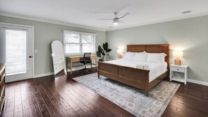 Ein Schlafzimmer mit einem hölzernen Bett, einem Schreibtisch, einem Stuhl, einem Deckenventilator und einem Fenster mit Jalousien.