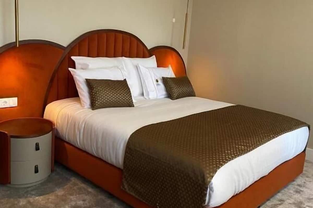 A modern bedroom with a large bed, a nightstand, and a wall-mounted lamp.