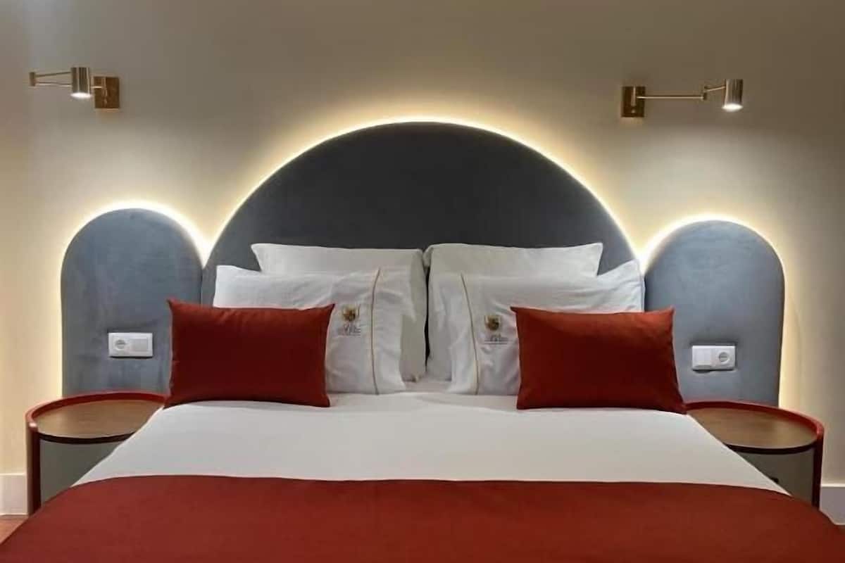 A modern hotel room with a large bed, two bedside tables, and a unique curved headboard.