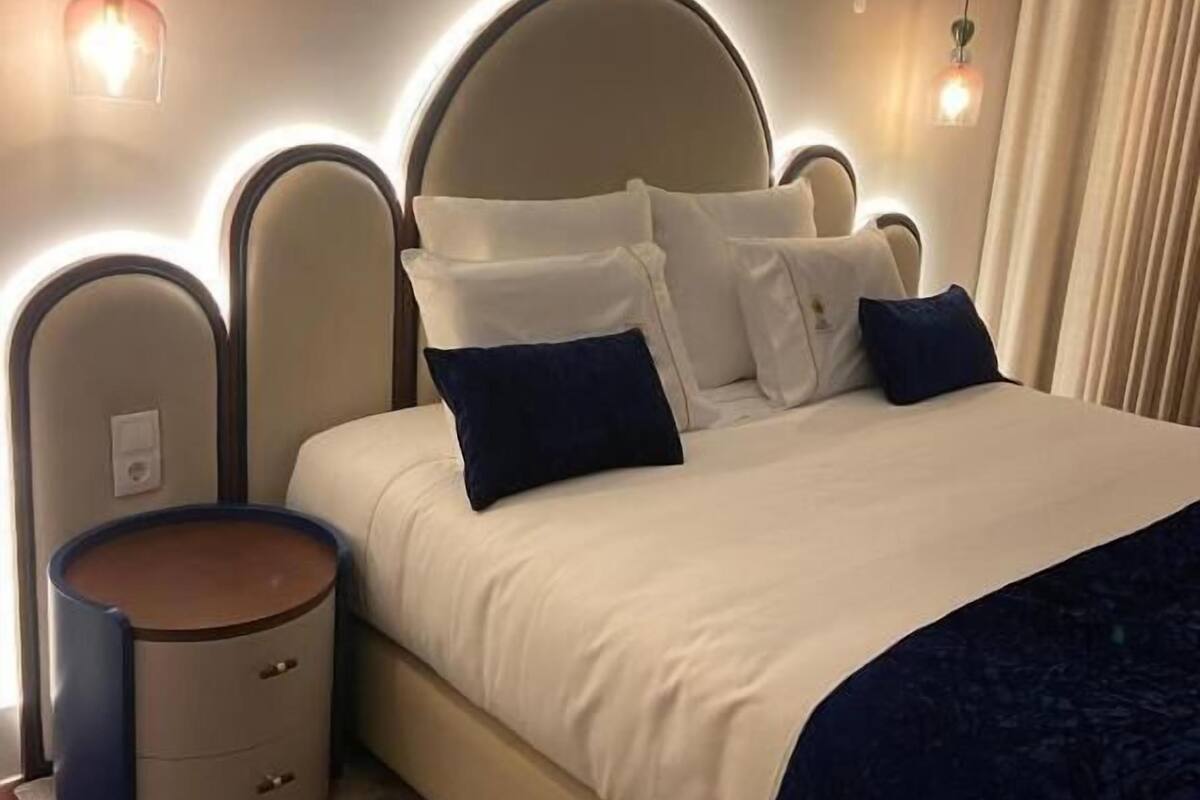 A neatly made bed with a headboard, a bedside table, and two wall-mounted lamps.