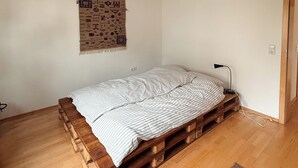 A room with a bed on a wooden pallet base, a wall hanging, a lamp, and a door. - Large, cozy vacation apartment in the heart of the Kraichgau. (Kraichtal)