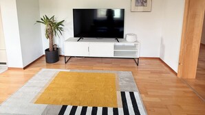 A living room with a flat-screen TV on a white entertainment unit, a potted plant, and a striped area rug. - Large, cozy vacation apartment in the heart of the Kraichgau. (Kraichtal)