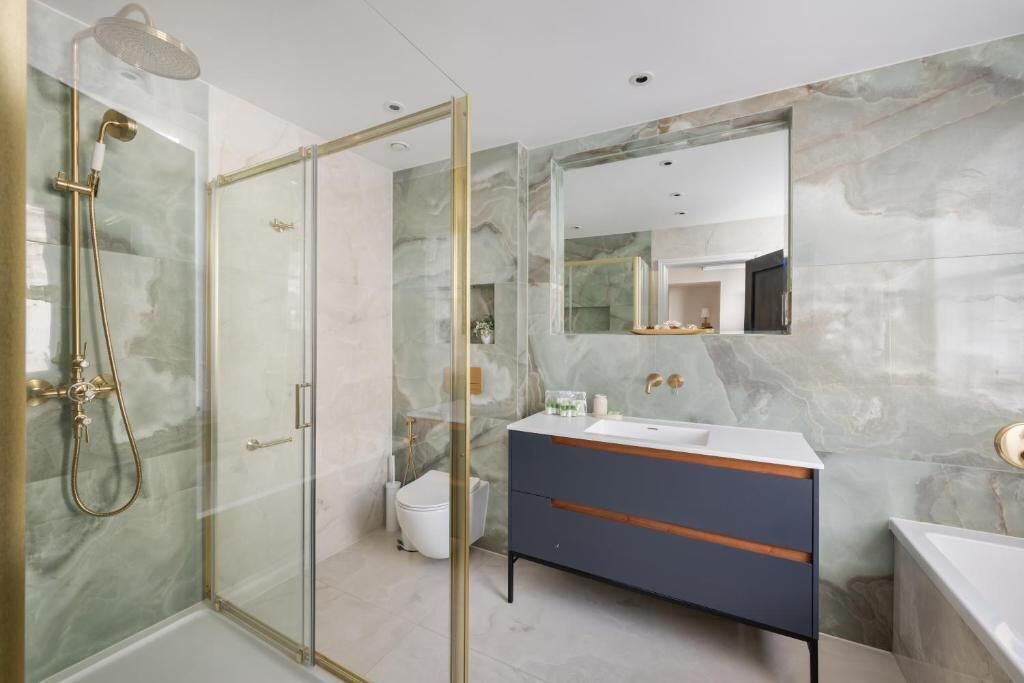 Ein modernes Badezimmer mit einer in Glas eingefassten Dusche, einer Marmorwand, einem Waschtisch und einem großen Spiegel.