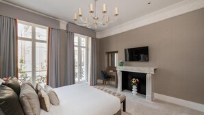 A spacious bedroom with a large bed, a fireplace, a desk, and a television.