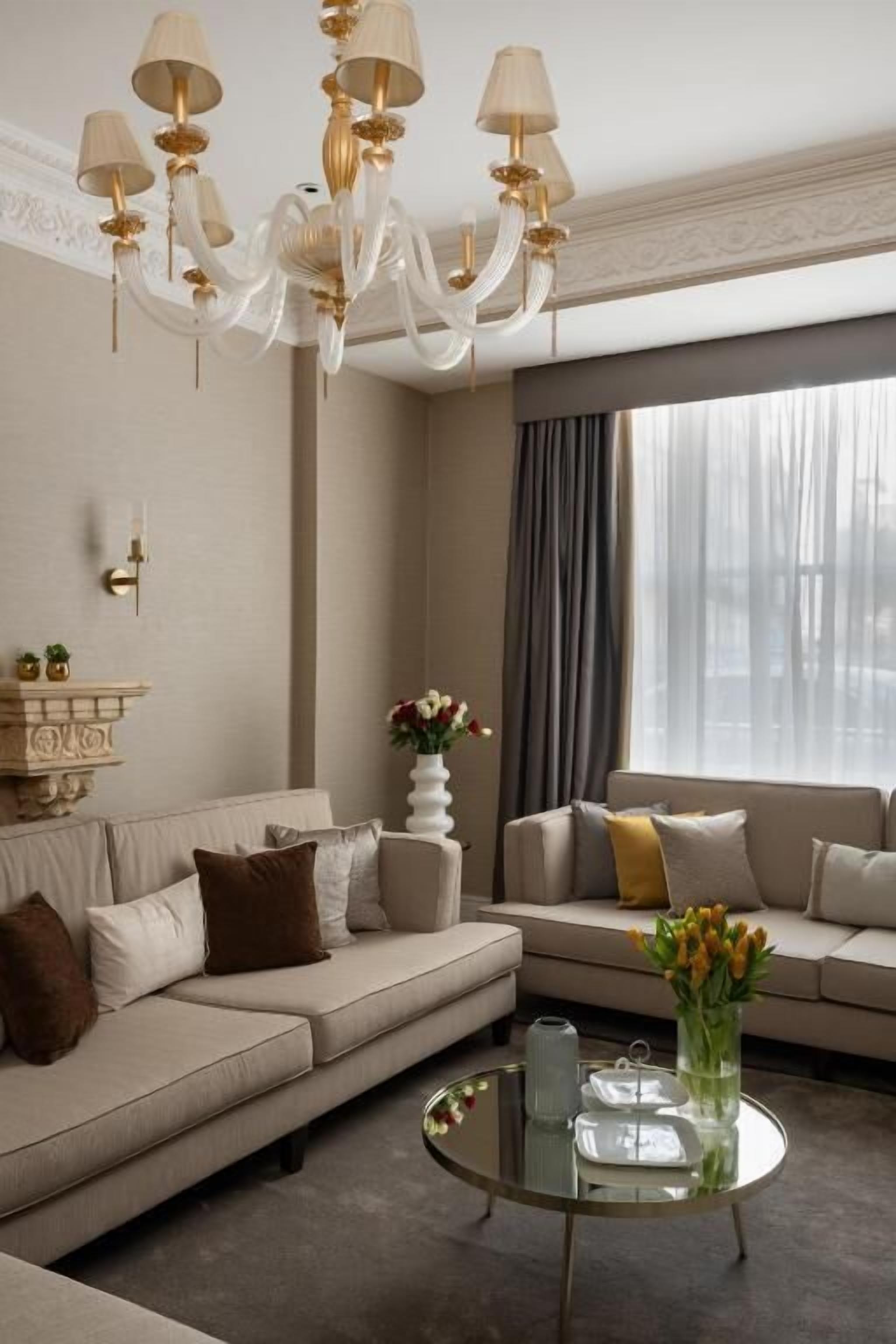 A modern living room with a beige sofa, a glass coffee table, and a chandelier.