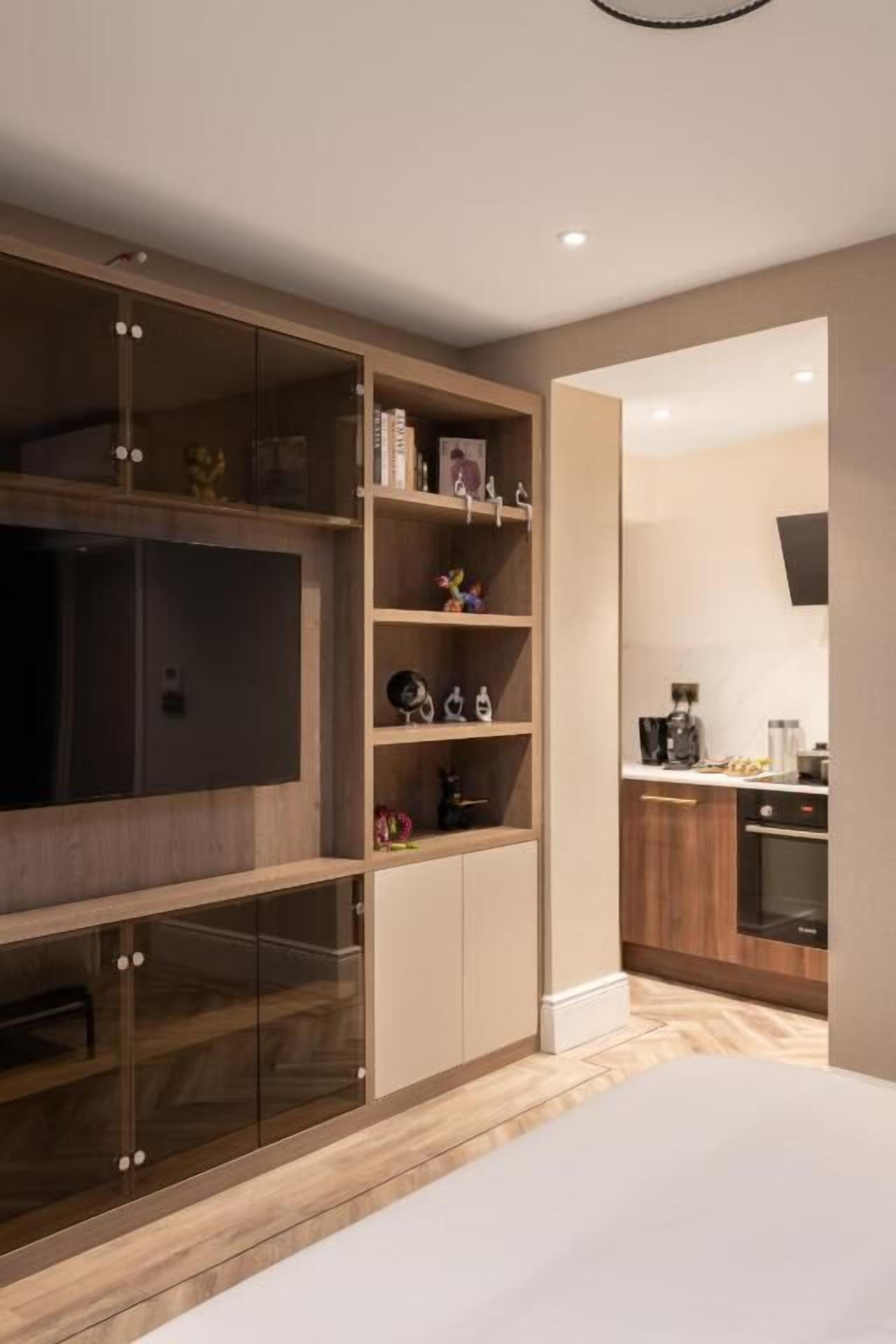 A modern bedroom with a large bed, a built-in TV, and a wooden wardrobe with glass doors.