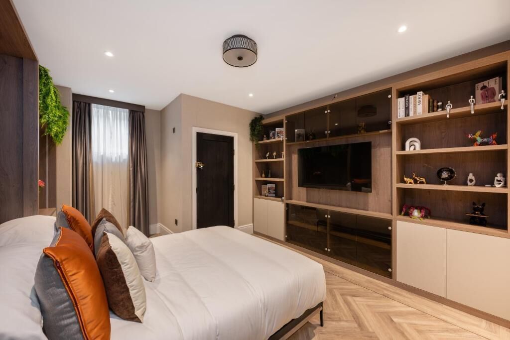 A bedroom with a large bed, a TV, and built-in shelving with various items.