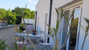 A modern outdoor patio with a dining table and chairs, surrounded by potted plants and a white building with large windows. - Superb T4 80m2 - Terrace 40m2 - 4/6pers - fully equipped and linen included (Vannes)